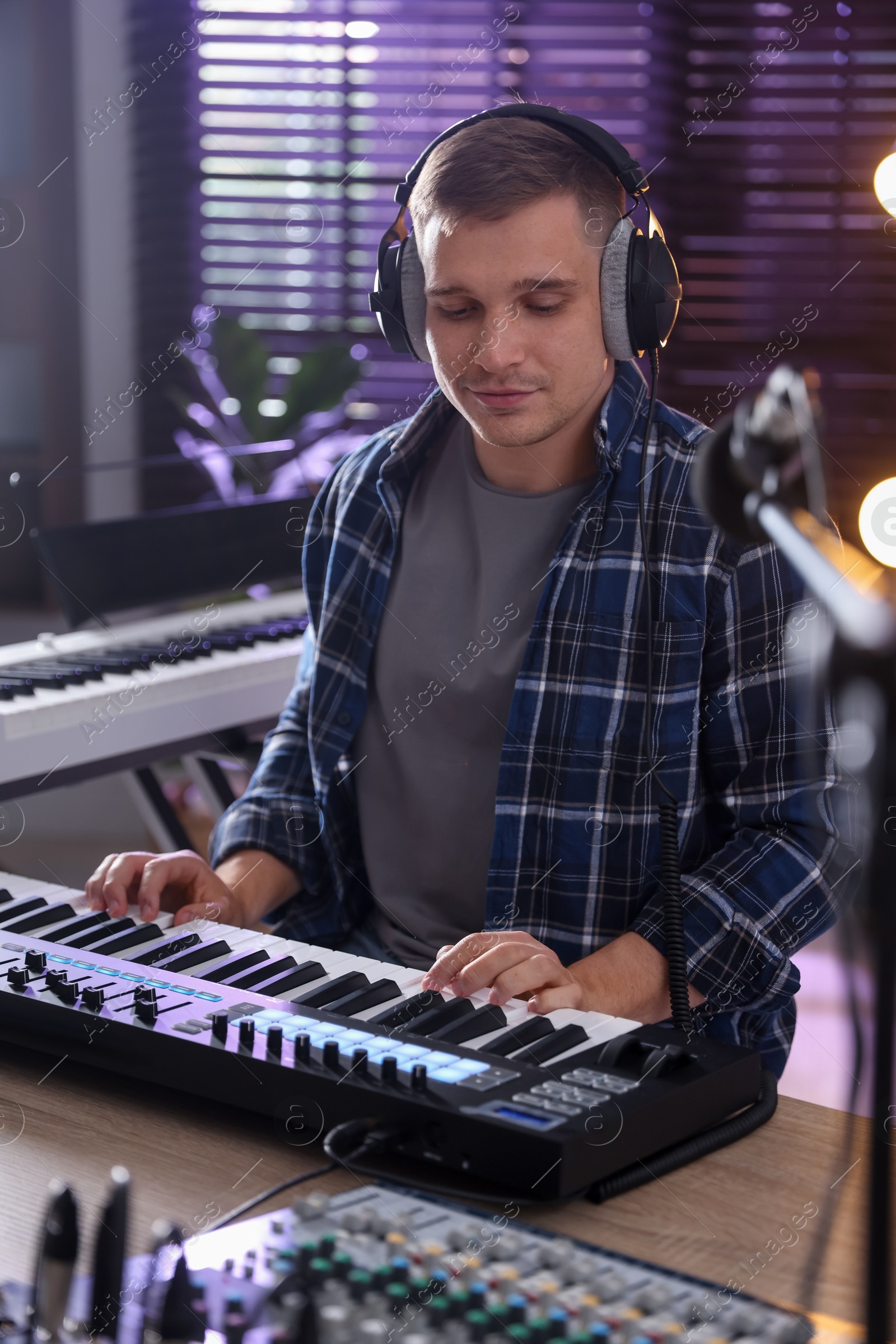 Photo of Man in headphones working with MIDI keyboard at table in home studio