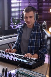 Photo of Man in headphones working with MIDI keyboard at table in home studio