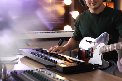 Photo of Man working with MIDI keyboard and guitar at table, closeup