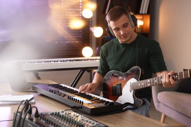Photo of Man in headphones working with MIDI keyboard and guitar at table in home studio