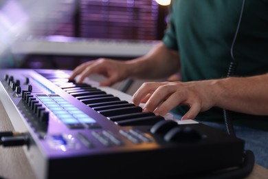 Photo of Man working with MIDI keyboard at table indoors, closeup