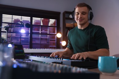 Photo of Smiling man in headphones working with MIDI keyboard at table in home studio, low angle view