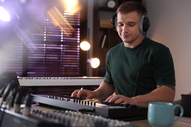 Photo of Man in headphones working with MIDI keyboard at table in home studio