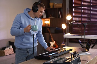 Photo of Man in headphones working with MIDI keyboard at table in home studio