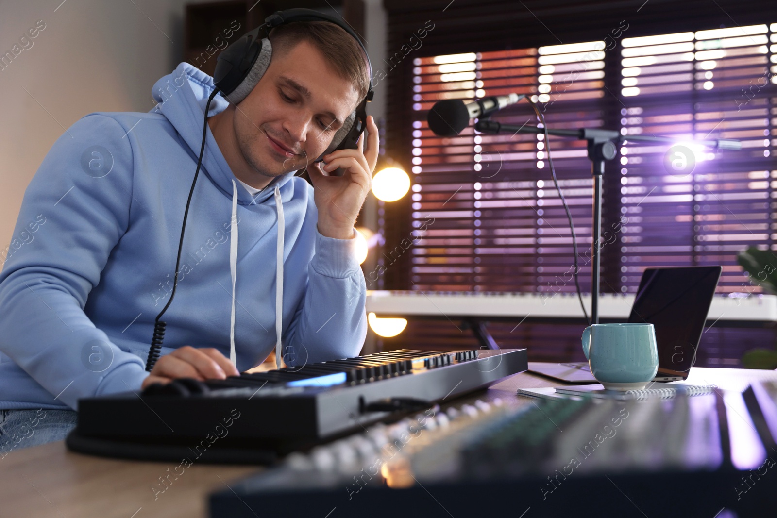 Photo of Man in headphones working with MIDI keyboard at table in home studio, low angle view