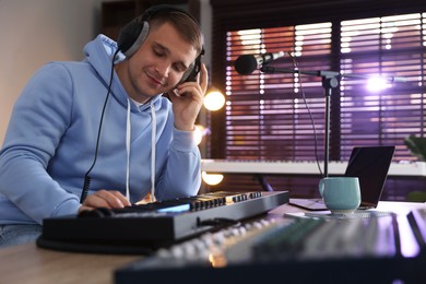 Photo of Man in headphones working with MIDI keyboard at table in home studio, low angle view