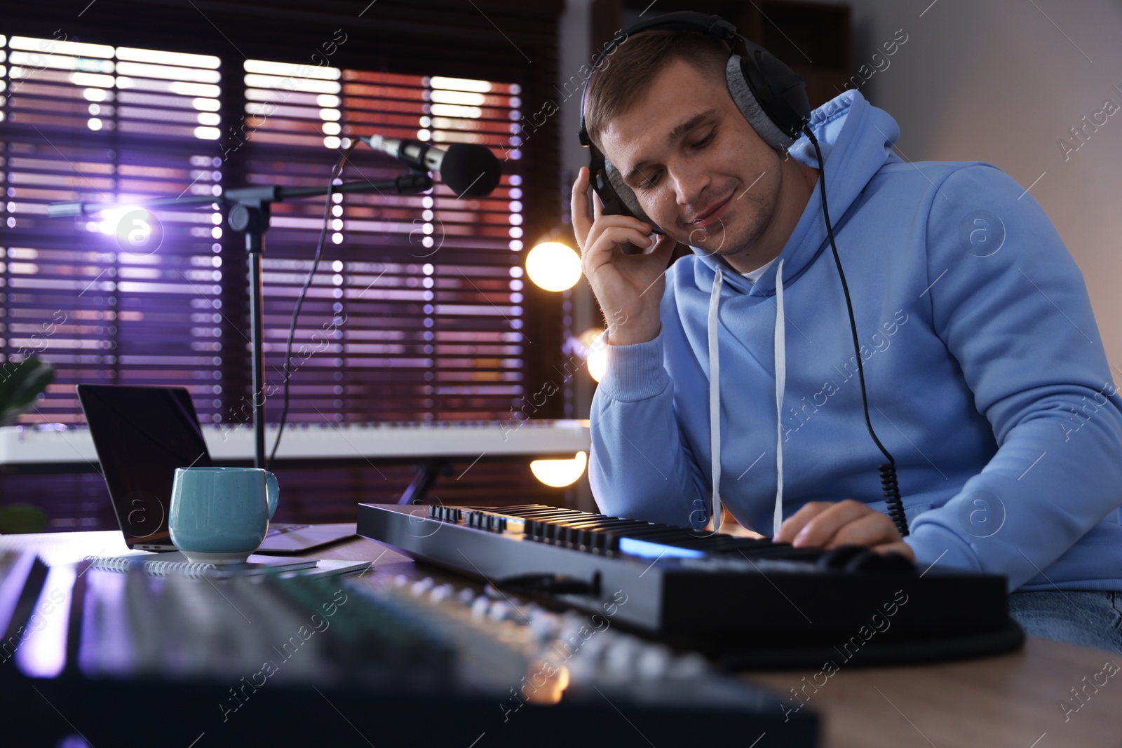 Photo of Man in headphones working with MIDI keyboard at table in home studio, low angle view