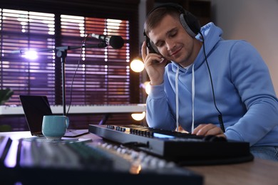 Photo of Man in headphones working with MIDI keyboard at table in home studio, low angle view
