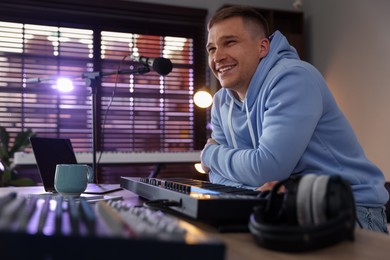 Photo of Smiling man working with MIDI keyboard at table in home studio, low angle view
