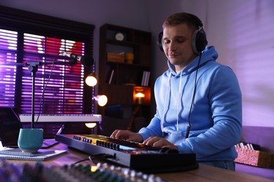 Photo of Man in headphones working with MIDI keyboard at table in home studio, low angle view