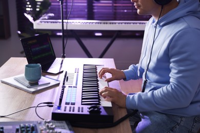 Photo of Man working with MIDI keyboard at table in home studio, closeup