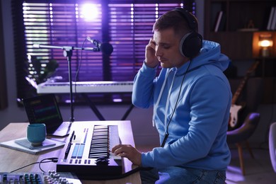 Photo of Man in headphones working with MIDI keyboard at table in home studio
