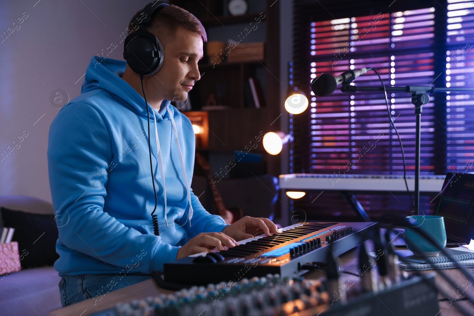 Photo of Man in headphones working with MIDI keyboard at table in home studio