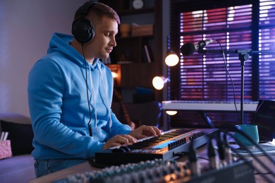 Photo of Man in headphones working with MIDI keyboard at table in home studio
