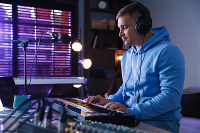 Photo of Man in headphones working with MIDI keyboard at table in home studio