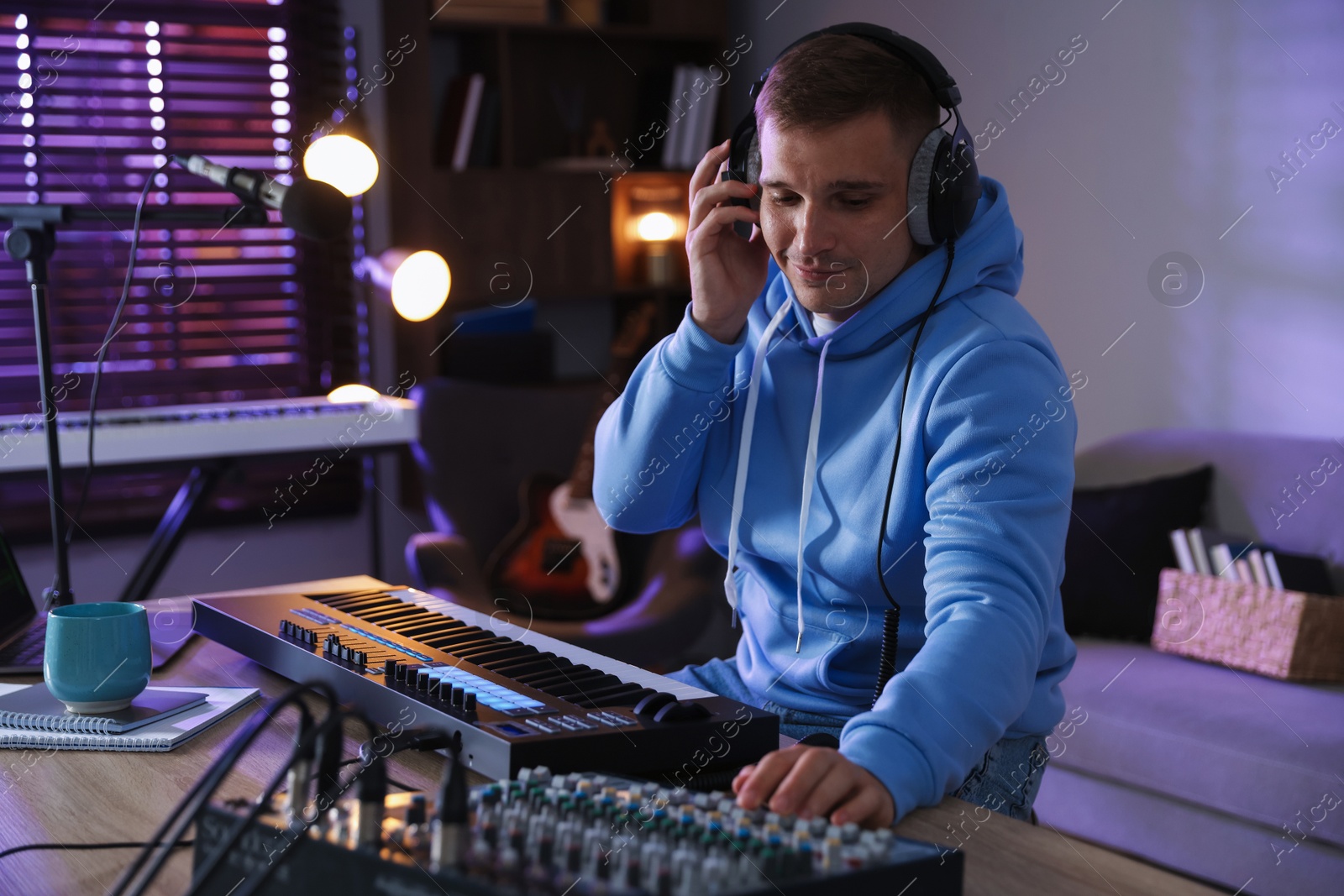 Photo of Man in headphones working with MIDI keyboard and dj mixer at table in home studio