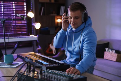 Photo of Man in headphones working with MIDI keyboard and dj mixer at table in home studio