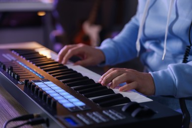 Photo of Man working with MIDI keyboard at table in home studio, closeup