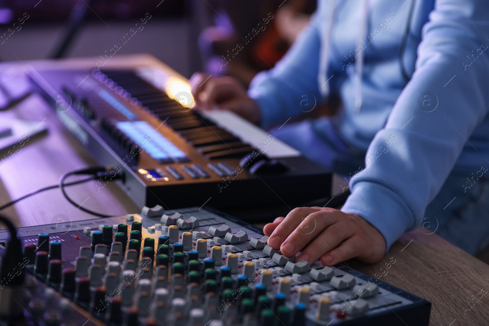 Photo of Man working with MIDI keyboard and dj mixer at wooden table in home studio, selective focus