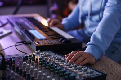 Photo of Man working with MIDI keyboard and dj mixer at wooden table in home studio, selective focus