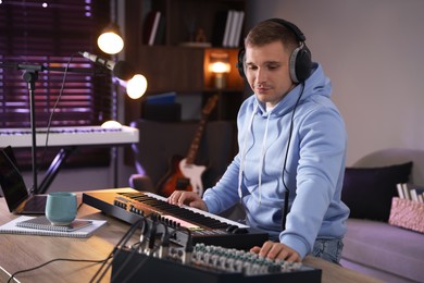 Photo of Man in headphones working with MIDI keyboard and dj mixer at table in home studio