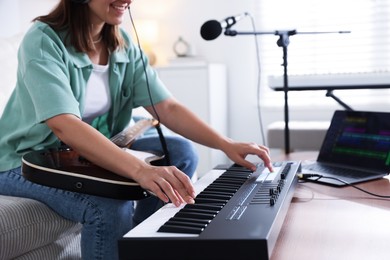 Photo of Smiling woman working with MIDI keyboard and guitar at table in home studio, closeup