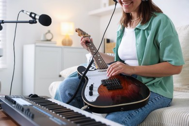 Photo of Smiling woman working with MIDI keyboard and guitar at table in home studio, closeup