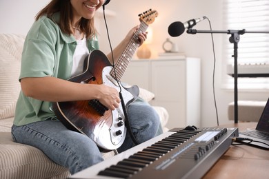Photo of Smiling woman working with MIDI keyboard and guitar at table in home studio, closeup