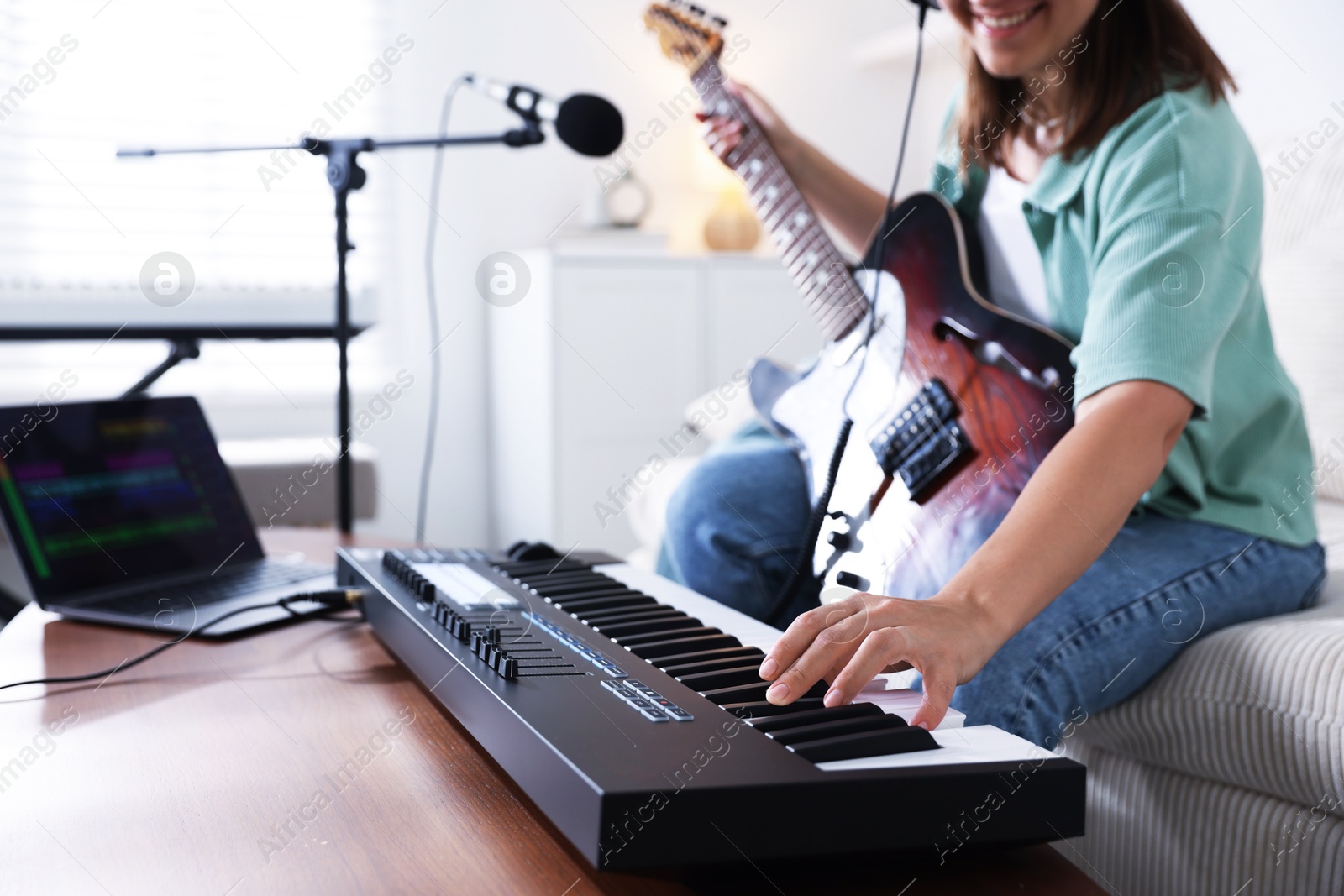 Photo of Smiling woman working with MIDI keyboard and guitar at table in home studio, selective focus