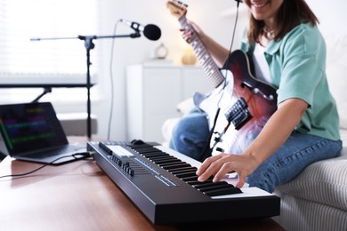 Photo of Smiling woman working with MIDI keyboard and guitar at table in home studio, selective focus