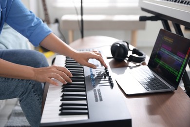 Photo of Woman working with MIDI keyboard at table indoors, closeup