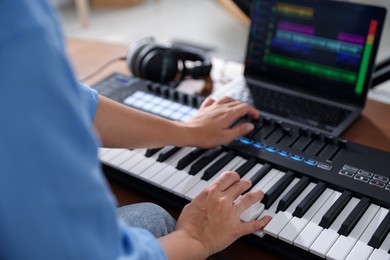 Photo of Woman working with MIDI keyboard at table indoors, closeup