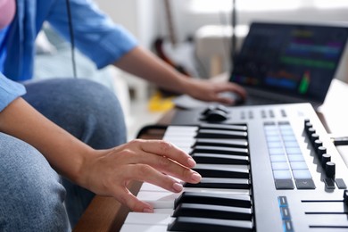 Photo of Woman working with MIDI keyboard and laptop at table indoors, selective focus