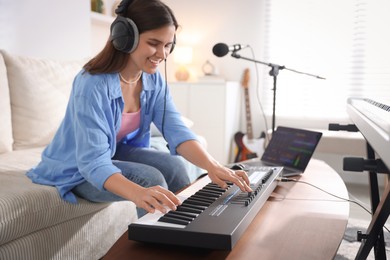 Photo of Smiling woman in headphones working with MIDI keyboard at table in home studio