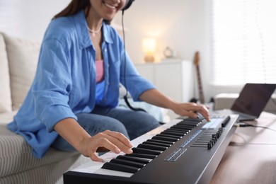 Photo of Smiling woman working with MIDI keyboard at table in home studio, closeup