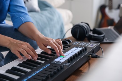 Photo of Woman working with MIDI keyboard at table indoors, closeup