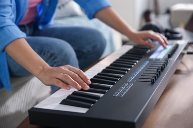 Photo of Woman working with MIDI keyboard at table indoors, closeup