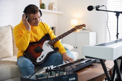 Photo of Man in headphones working with MIDI keyboard and guitar at table in home studio