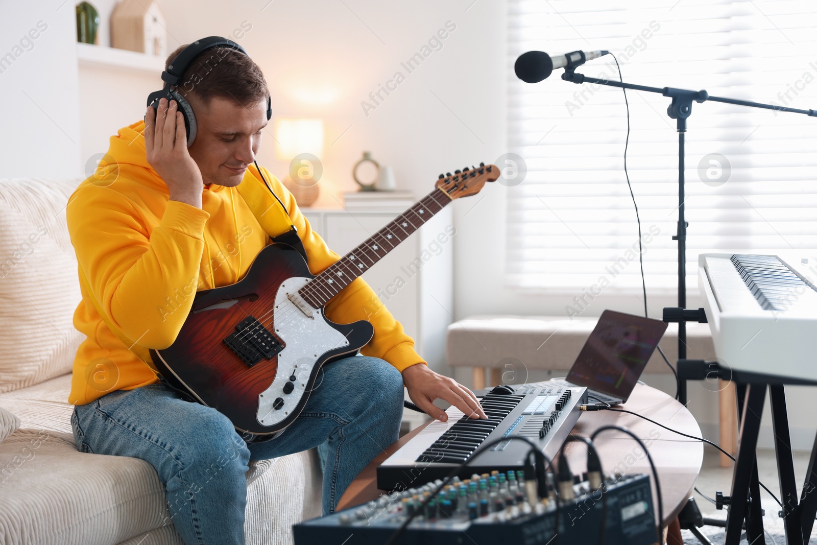 Photo of Man in headphones working with MIDI keyboard and guitar at table in home studio