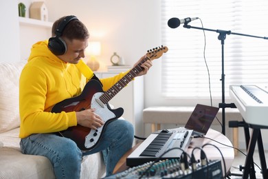 Photo of Man in headphones working with guitar and MIDI keyboard at table in home studio