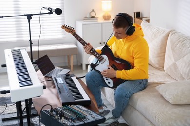 Photo of Man in headphones working with guitar and MIDI keyboard at table in home studio
