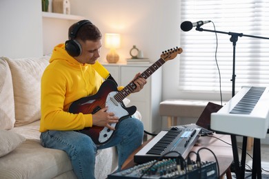 Photo of Man in headphones working with guitar and MIDI keyboard at table in home studio