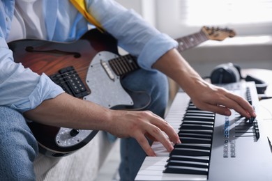 Photo of Man working with MIDI keyboard and guitar indoors, closeup