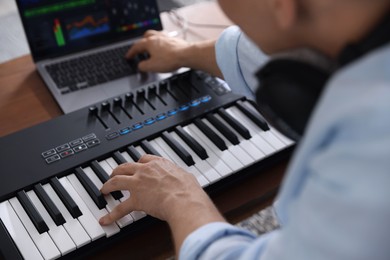 Photo of Man working with MIDI keyboard and laptop at table indoors, selective focus