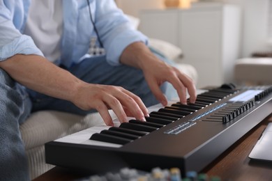 Photo of Man working with MIDI keyboard at table indoors, closeup