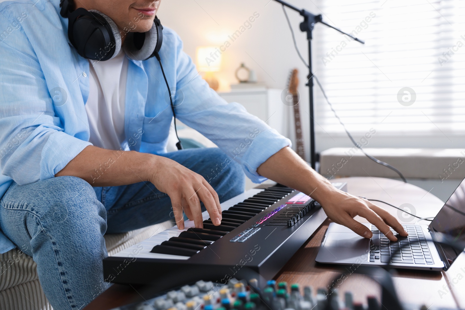 Photo of Man working with MIDI keyboard and laptop at table indoors, closeup