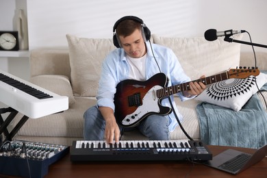 Photo of Man in headphones working with guitar and MIDI keyboard at table in home studio