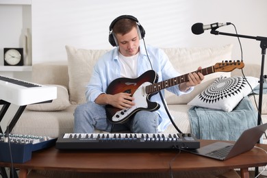 Photo of Man in headphones working with guitar and MIDI keyboard at table in home studio