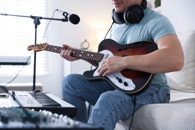 Photo of Man working with guitar and MIDI keyboard on sofa in home studio, closeup