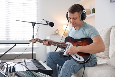 Photo of Man in headphones working with guitar and MIDI keyboard on sofa in home studio